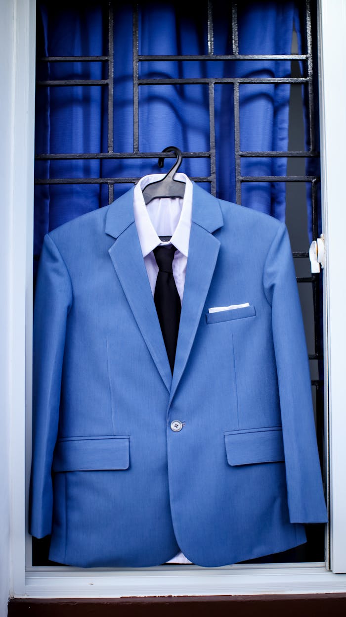 Classy light blue suit on hanger with black tie and white shirt placed on window bars